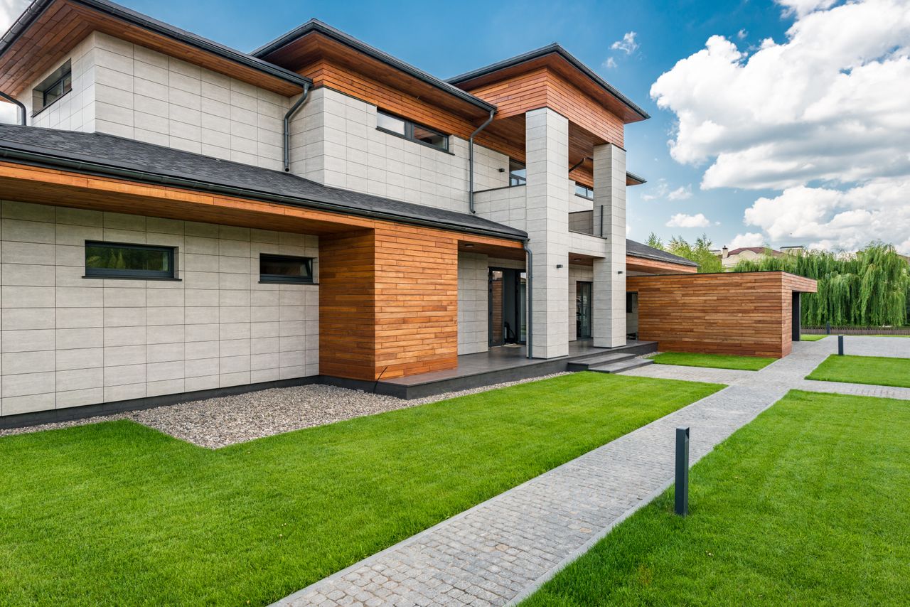 Exterior of contemporary residential house with green lawn and paths in sunny day
