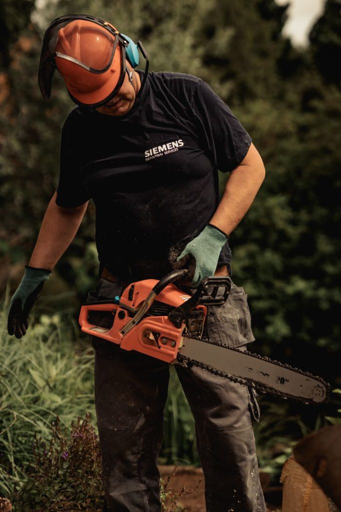 Man operating a chainsaw outdoors with safety gear in a forest environment.